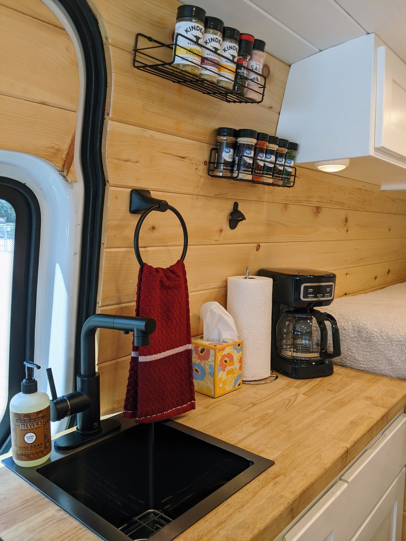 Inside this cozy RV rental, a compact kitchen offers wood paneling, a black sink, coffee maker, and neatly organized spices.
