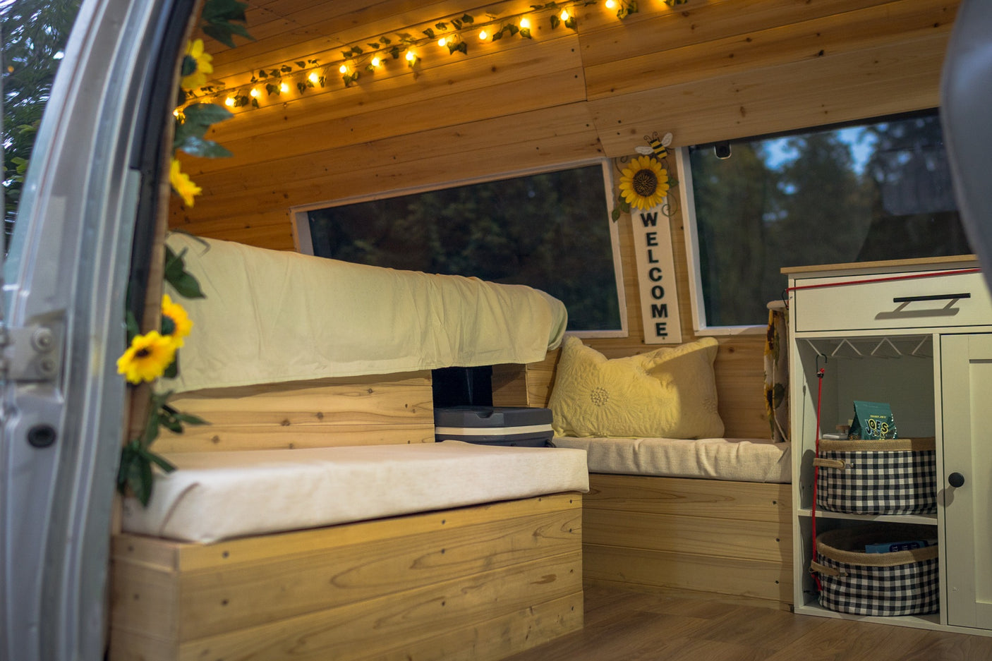 Step into this inviting RV rental: a custom wood interior with a bed, bench, storage, and cheerful sunflower decor.