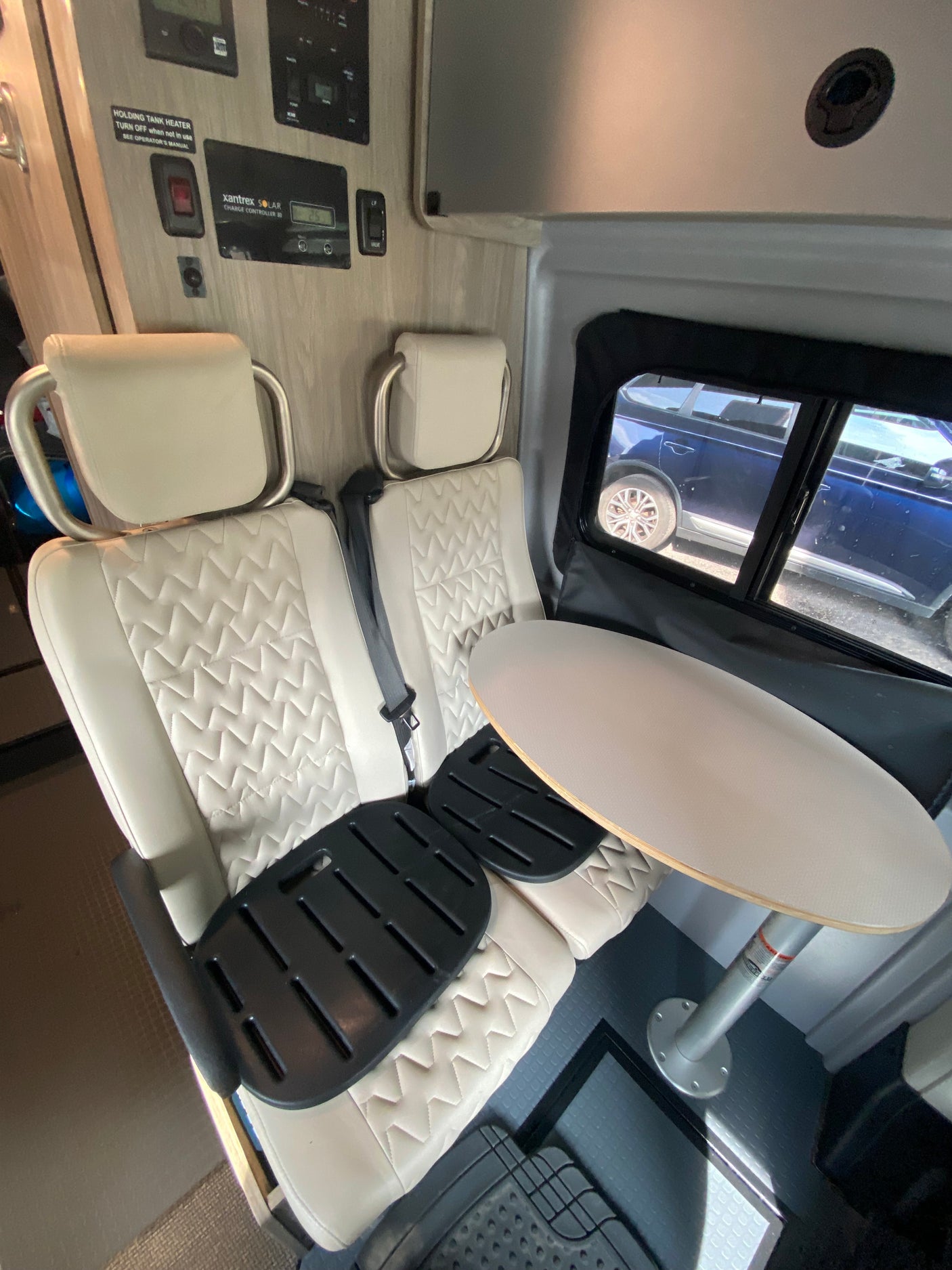 RV rental interior: Cream quilted seats, round table, and a control panel with holding tank heater & Xantrex solar controller.