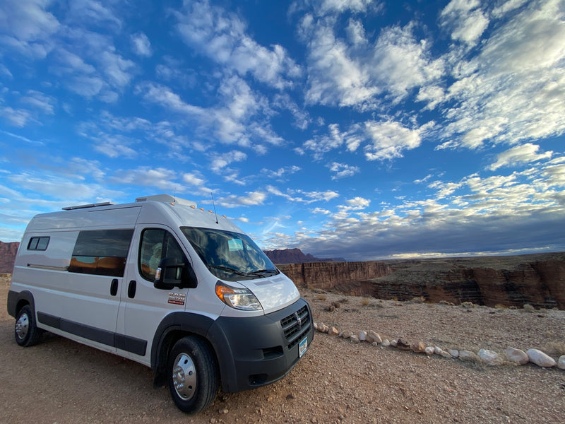 Explore epic canyons with an RV rental! This white camper van is parked overlooking a vast, rugged canyon under a dynamic sky. — photo 9
