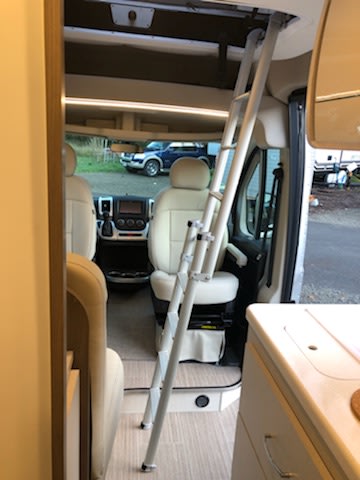 Inside this cozy RV rental, a ladder leads to an upper bunk, ready for adventure. Driver's cabin and kitchen visible. — photo 9