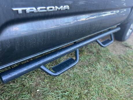 Wet Toyota Tacoma truck, dark paint & sturdy steps on grass. Ready for rugged use alongside your RV rental adventure!