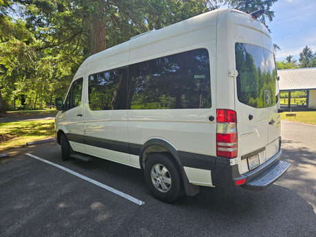 This white Mercedes Sprinter van RV rental is parked in a sunny, tree-lined park, perfect for your next camping trip.