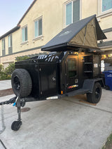 A sleek black off-road trailer with a deployed rooftop tent, a prime RV rental for your overland camping adventure awaits.