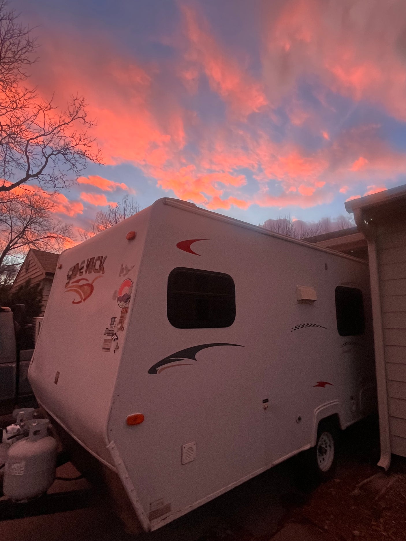 A vibrant pink and orange sunset illuminates a parked travel trailer. Discover your next adventure with an RV rental.