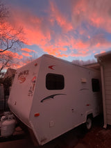 A vibrant pink and orange sunset illuminates a parked travel trailer. Discover your next adventure with an RV rental.