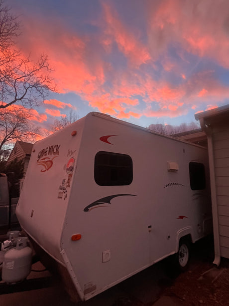 A vibrant pink and orange sunset illuminates a parked travel trailer. Discover your next adventure with an RV rental.