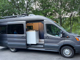 Gray RV rental van with an open side door, revealing its modern kitchen and a person inside. Solar panels are on the roof.