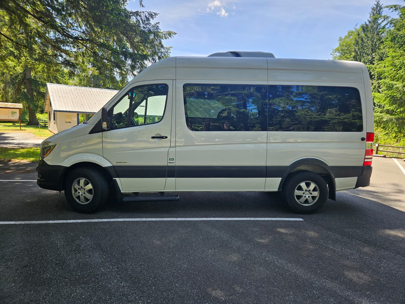 White Mercedes Sprinter RV rental van parked on asphalt in a wooded setting.