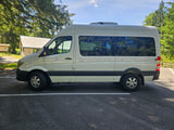 White Mercedes Sprinter RV rental van parked on asphalt in a wooded setting.