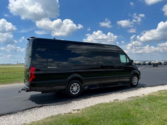 Luxury black Mercedes-Benz Sprinter van, ideal for RV rental, parked at an airfield on a bright, cloudy day.