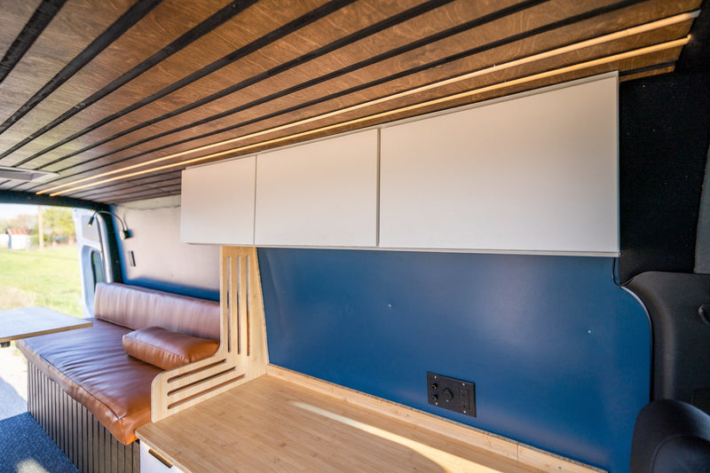 Inside a stylish RV rental: wood slat ceiling with ambient light, white overhead cabinets, blue panel, and brown leatherette seating. — photo 16