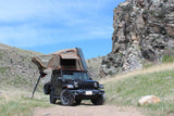 Adventure awaits! This black Jeep with a deployed rooftop tent, an alternative to an RV rental, is ready for off-road camping.