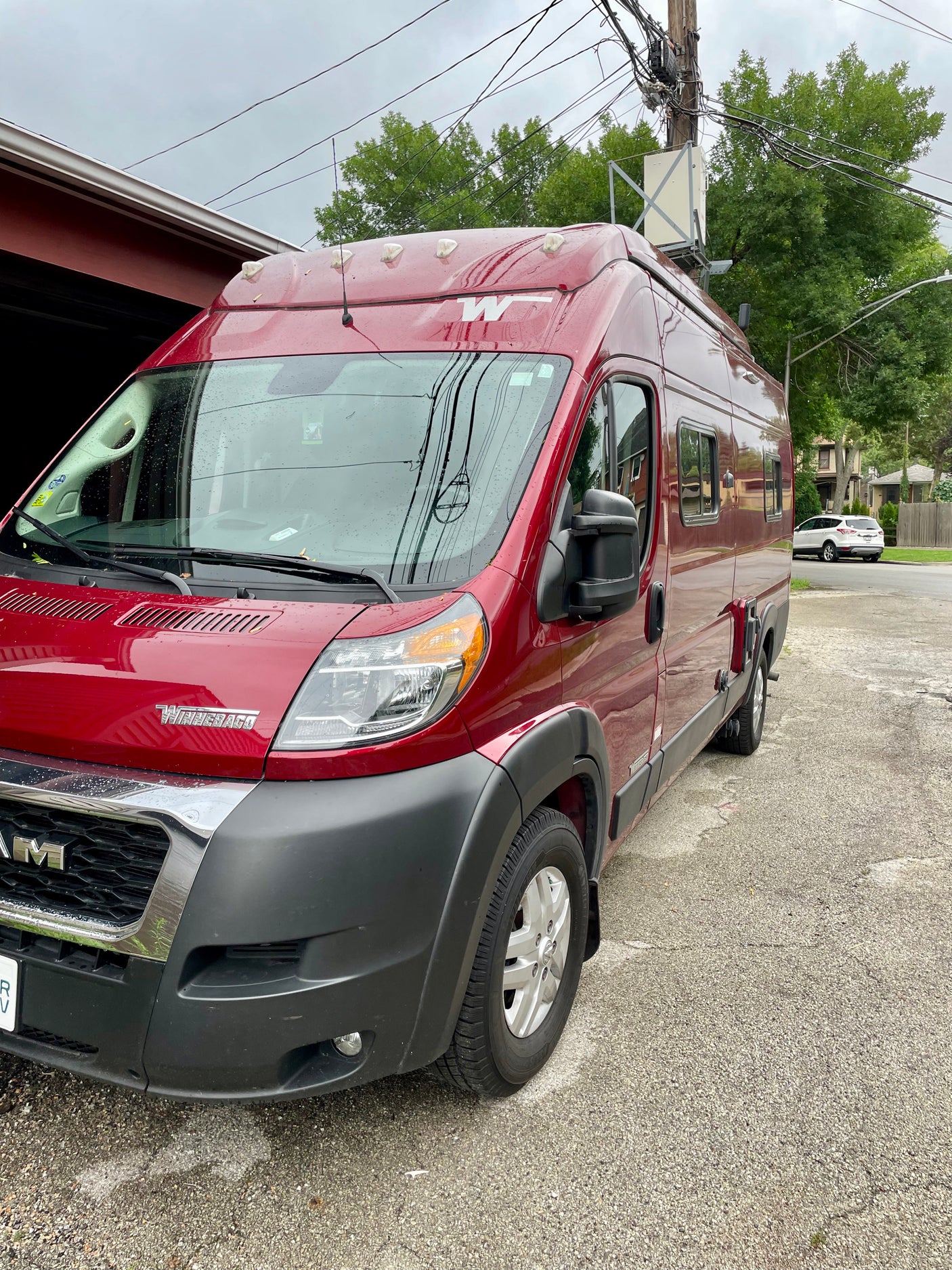 A vibrant red Winnebago camper van, possibly an RV rental, parked on a driveway.