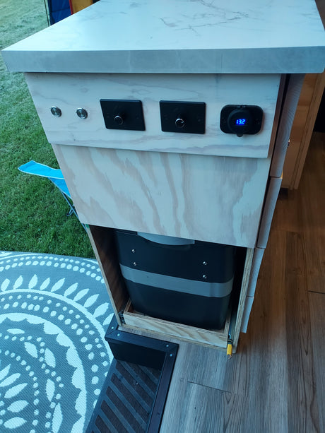Inside an RV rental: a custom pull-out storage unit with electrical controls (13.2V display) and a large water tank.