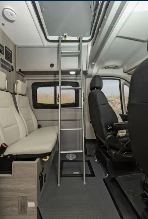 Spacious RV rental interior featuring flexible seating, an overhead bunk bed via ladder, and front cabin area for travel. — photo 17