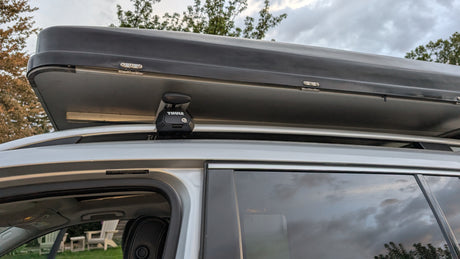 Black Thule roof cargo box on a silver car's roof rack, seen from the side. Ideal for RV rental trips or extra travel storage.