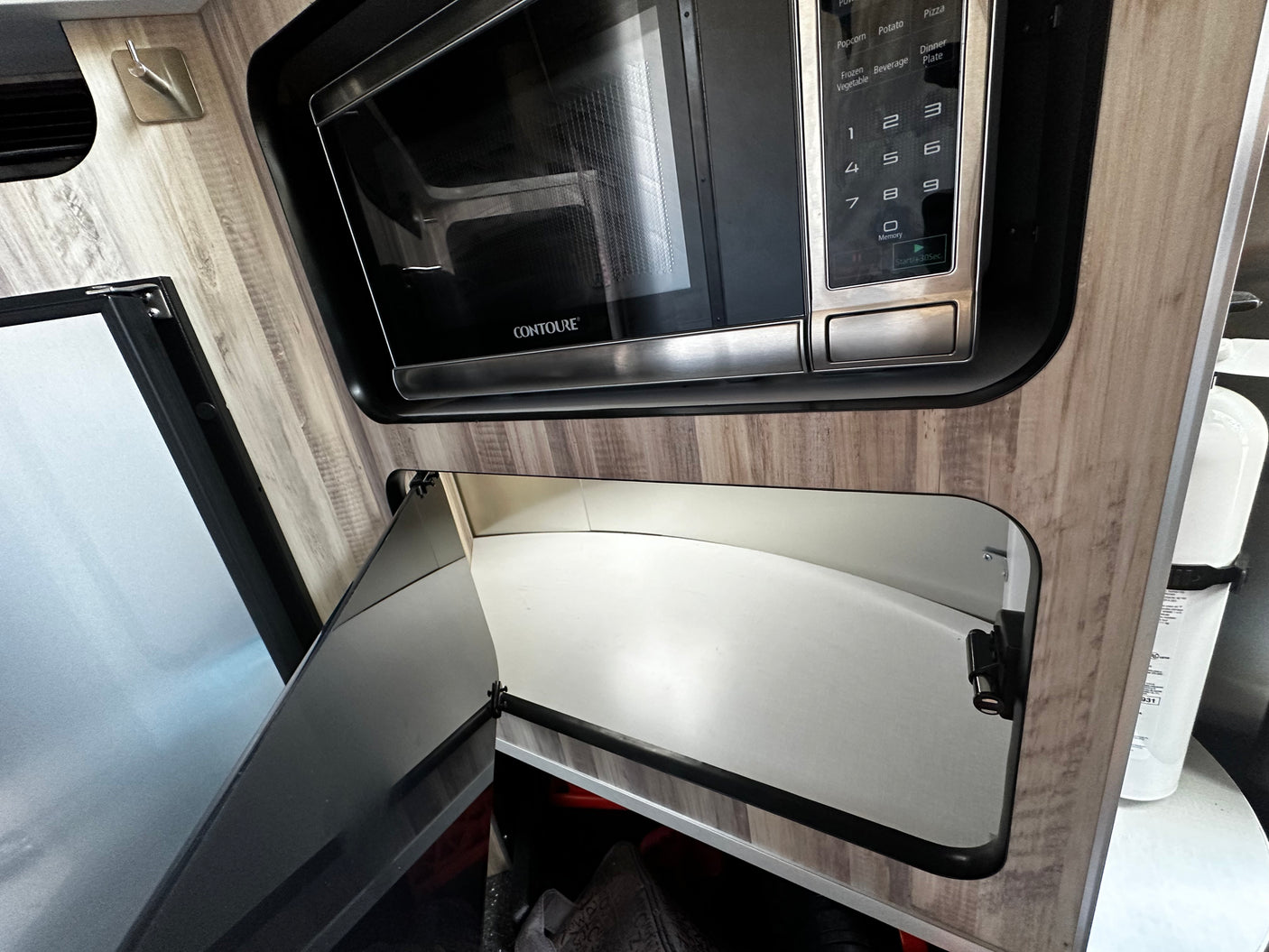 Interior of an RV rental showing a CONTOURE microwave over an open cabinet, with a refrigerator and fire extinguisher.
