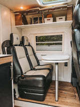 Cozy RV rental interior with comfortable two-tone seats, adjustable dining table, and overhead storage for organized travel.