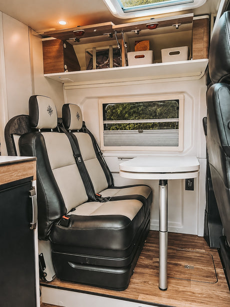Cozy RV rental interior with comfortable two-tone seats, adjustable dining table, and overhead storage for organized travel.