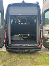 RV rental: Rear of a black camper van with open doors, showing a convertible black bench bed and storage space.