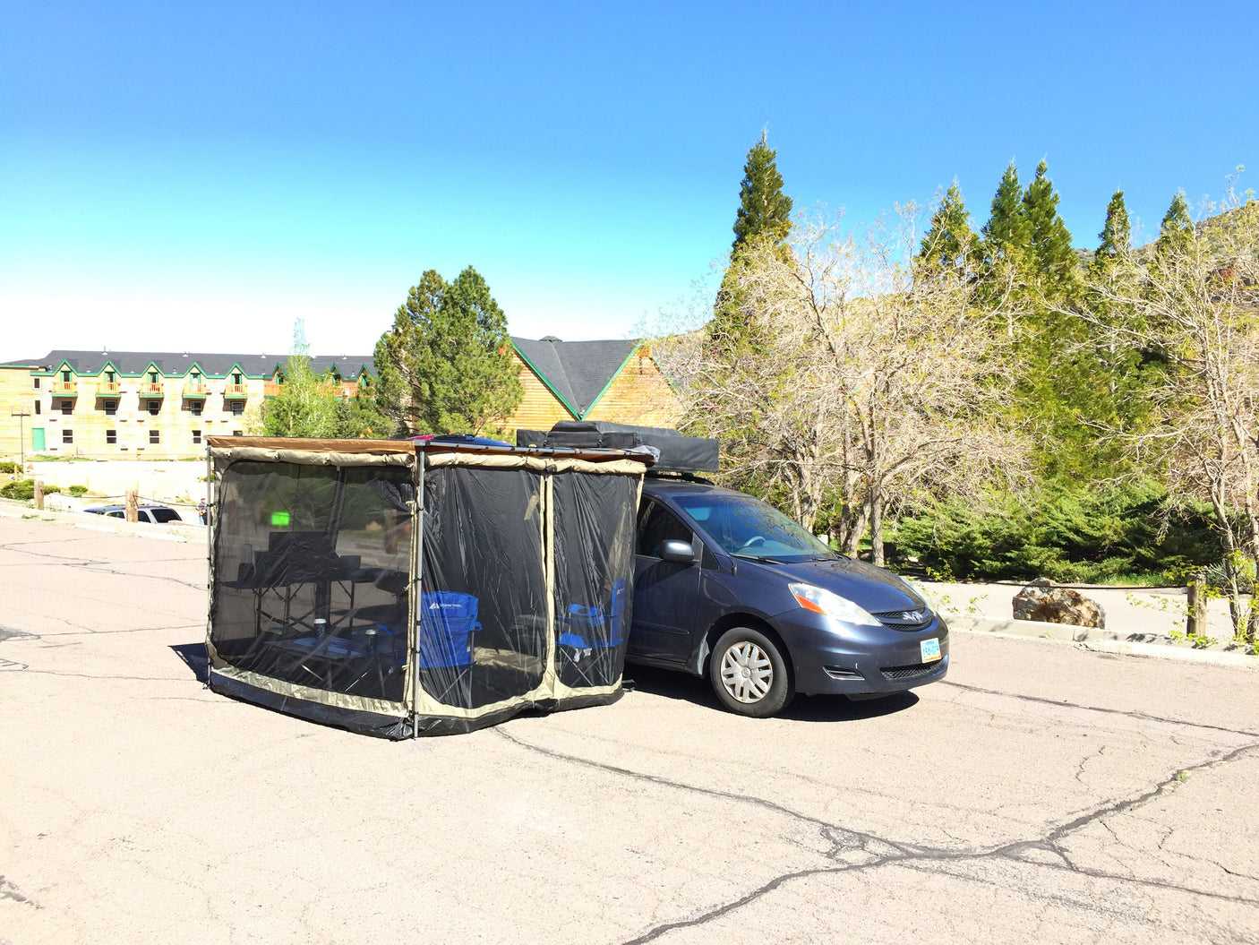 A unique RV rental experience: a minivan with an attached screen room, chairs, and table setup on pavement. Perfect for camping!