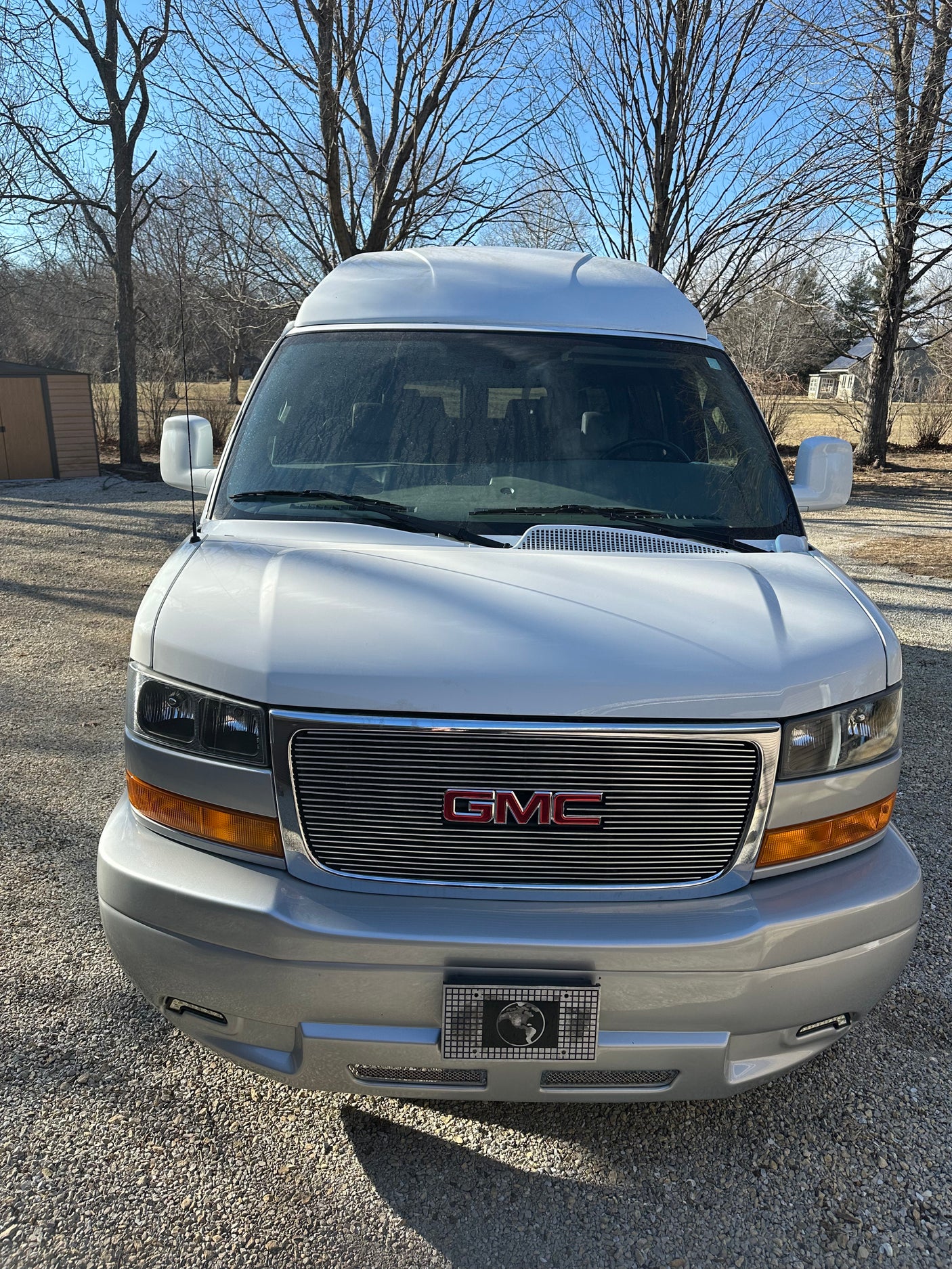 Front of a white GMC conversion van, suitable for rv rental. Features a high roof and chrome grille.