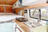 Step into this rv rental's compact interior: a comfy bed, kitchenette with sink & cooktop, and warm wood accents.