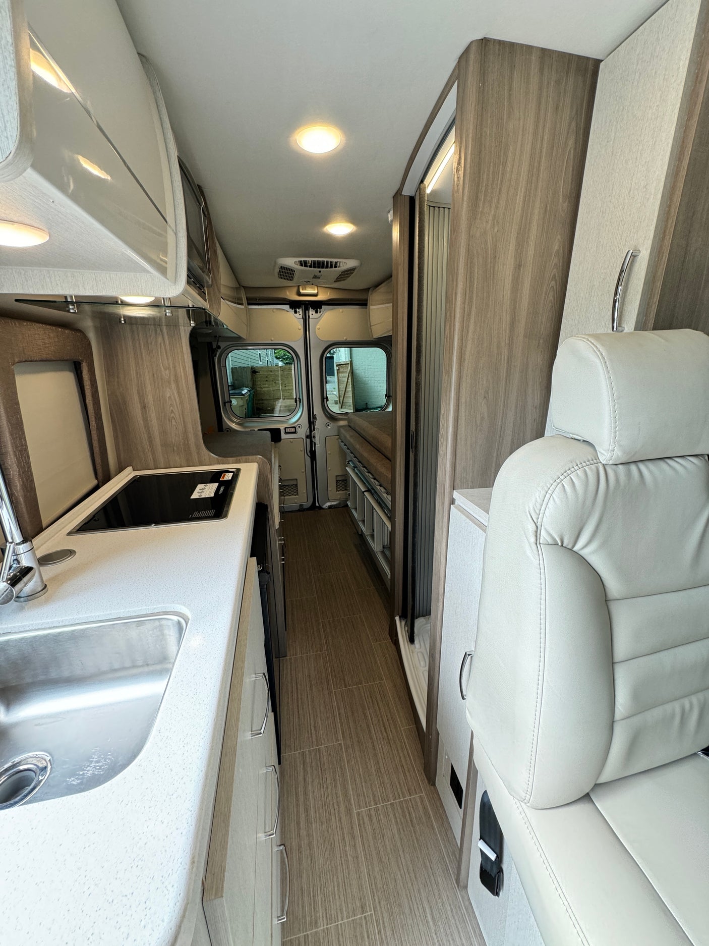 Modern RV rental interior showing kitchenette, light wood cabinetry, and a cozy living area with rear views.