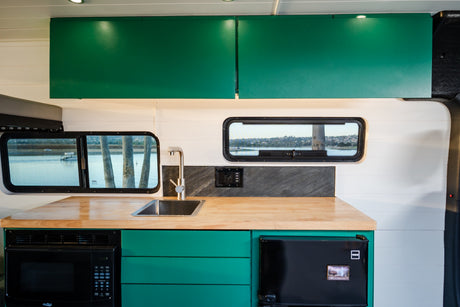 RV rental camper van's modern kitchen boasts wood counters, a sink, microwave, fridge, and teal cabinets for travel.