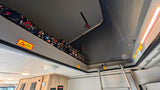 Elevated sleeping area inside an RV rental with pop-top roof, floral bedding, safety warnings & ladder.