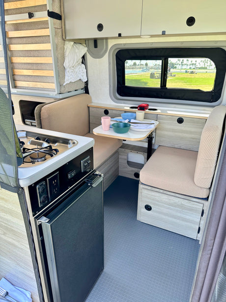 Cozy RV rental interior with compact kitchenette, dining, fridge, and a scenic window view.