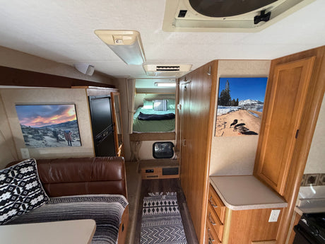 Cozy rv rental interior: main living area with brown couch, full bed, kitchen counter. Decorated with rugs & wall art.