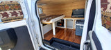 Explore this rv rental's cozy van interior: built-in bed, warm wood paneling, cooking stove, and integrated power system.