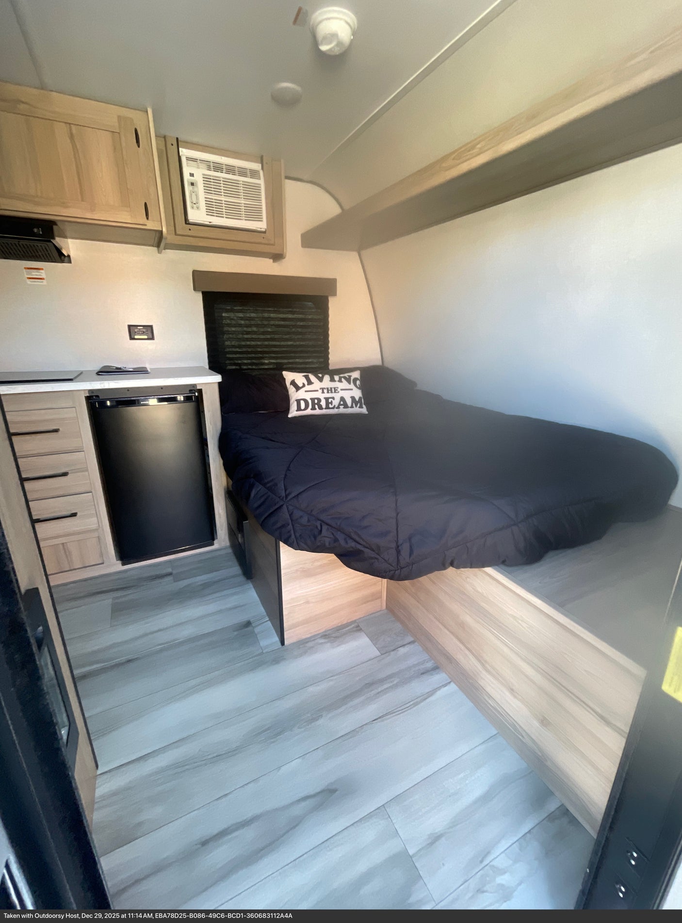 This RV rental interior features a cozy bed with a "LIVING THE DREAM" pillow, mini-fridge, AC, and storage.