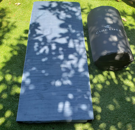 RV rental ready: A grey camping mattress and rolled gear bag on green artificial grass with tree shadows.