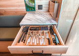 This RV rental features an open kitchen drawer revealing organized utensils, flatware, and cooking tools for efficient storage.