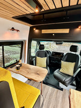 Spacious RV rental interior featuring vibrant yellow seating, live-edge wood table, and a sleek driver's cabin.