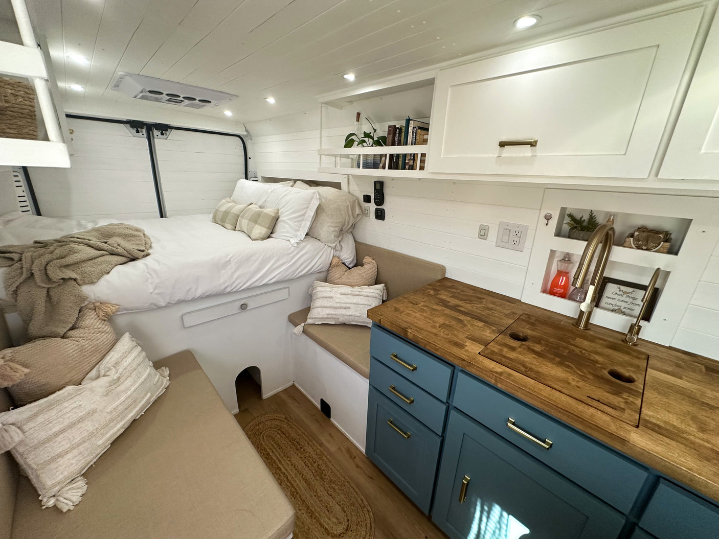 Bright rv rental interior featuring a bed, kitchenette with wooden counter and blue cabinets, plus cozy seating for mobile living.