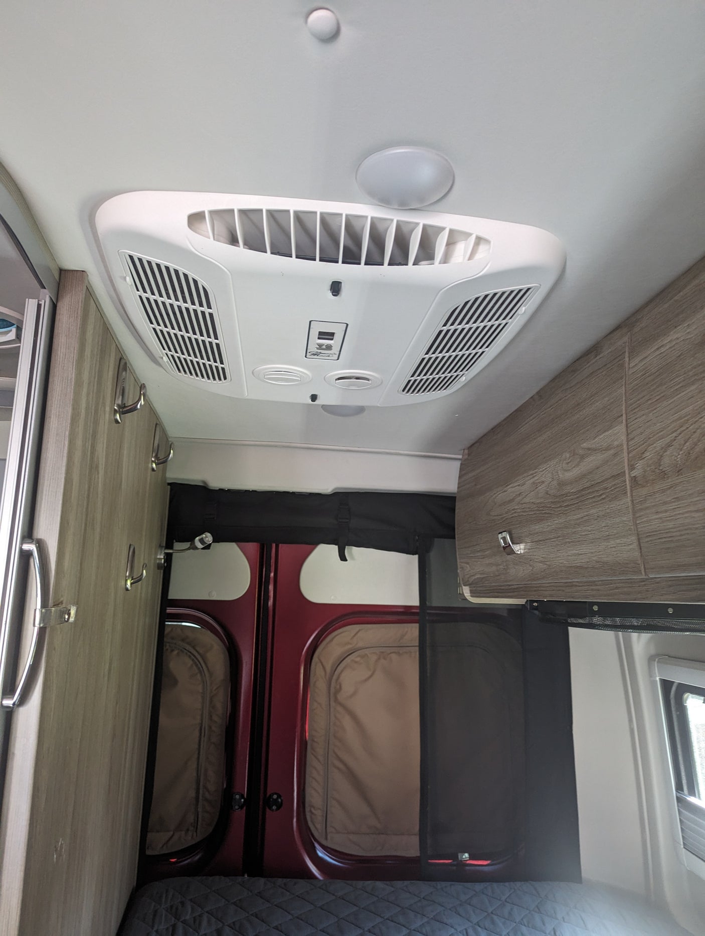 Overhead view in an rv rental showing a Dometic AC unit, ceiling lights, side cabinets with hooks, and rear doors with screens.