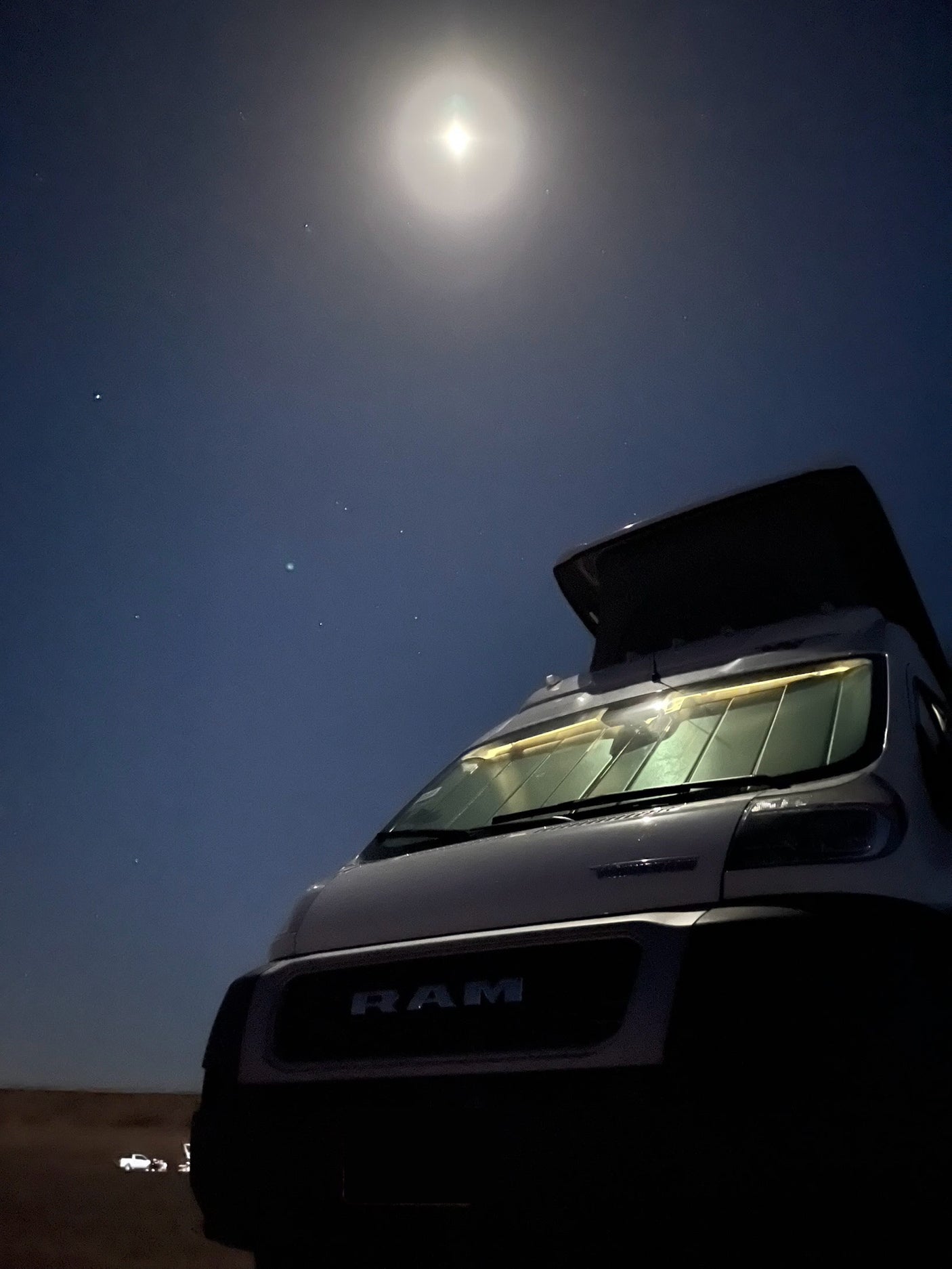 A RAM **RV rental** camper van with its pop-top open is bathed in bright moonlight under a clear night sky with stars.