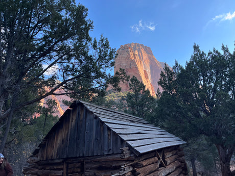 Rustic cabin surrounded by trees, with majestic red rock mountains in the background. Ideal scenic stop for your RV rental journey.
