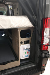 View inside an RV rental: Rear bed and integrated utility panel with water and power connections, plus storage.
