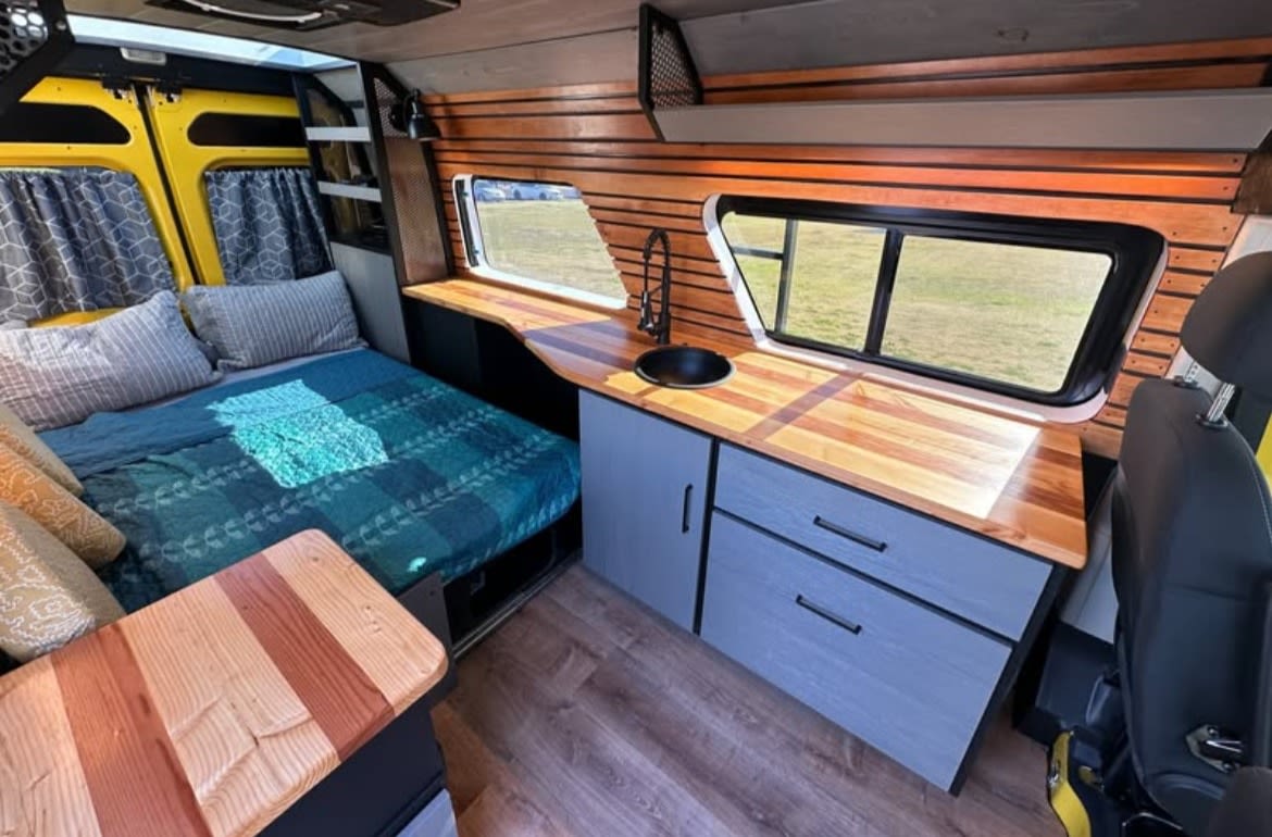 Spacious RV rental interior featuring a comfy bed, functional kitchen with wood counters, and scenic windows. — photo 6