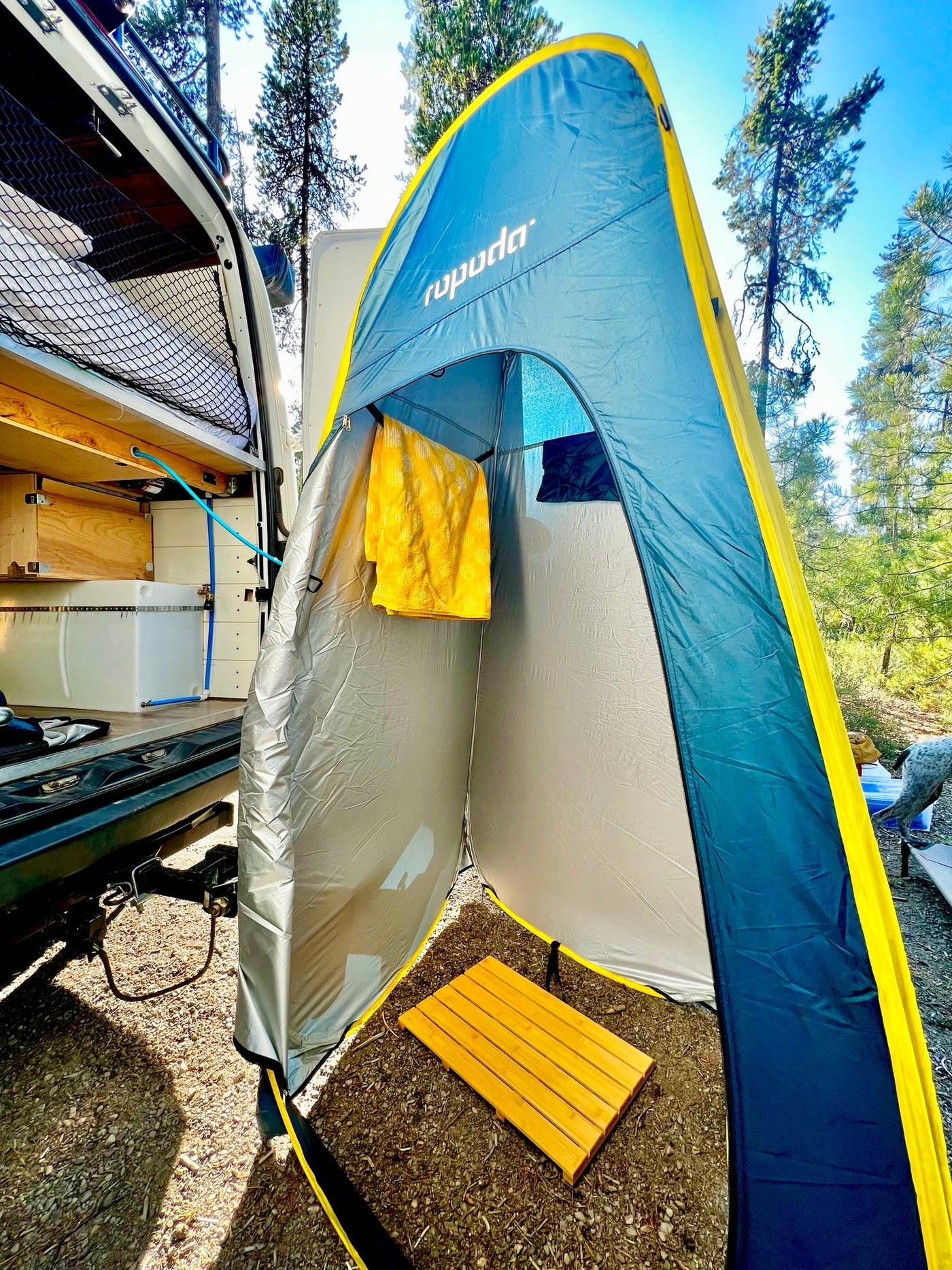 An RV rental with its rear doors open, showing an outdoor shower tent setup with a yellow towel & wooden mat. — photo 18