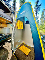 An RV rental with its rear doors open, showing an outdoor shower tent setup with a yellow towel & wooden mat.
