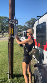 Woman hooking up an RV rental at campsite 42. She's connecting power to a white RV at a sunny campground.