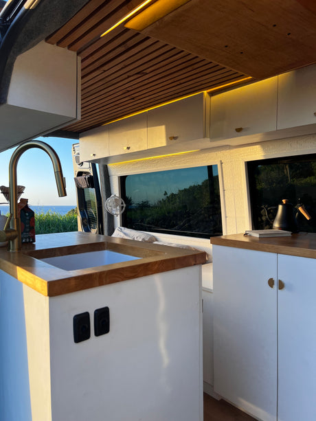 Luxurious RV rental interior featuring a bright kitchen, wood-slat ceiling with LED lights, and stunning ocean views.
