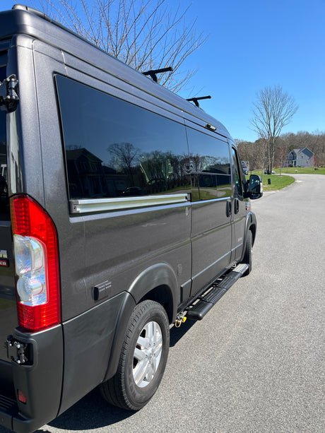 This dark gray RV rental, a modern camper van, is parked on an asphalt road under a clear blue sky, ready for adventure.