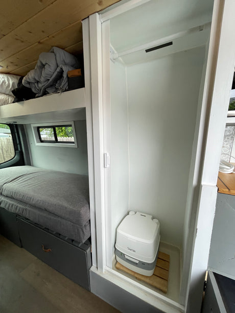 Experience an RV rental's clever interior: a comfortable bed, upper bunk, and a private area with a portable toilet.